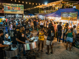 Night market scene in Buccoo Tobago at night with a steel drum band performing and crowded food stalls under string lights